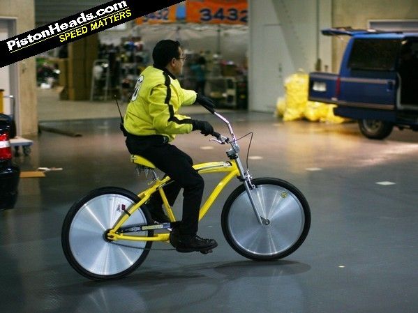 Mooneyes organiser Shige cycles past on a cruiser bike addressing everyone 